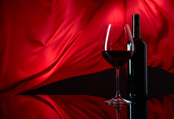 Skleněné víno a láhev červeného vína na černém reflexním backgrounu — Stock fotografie