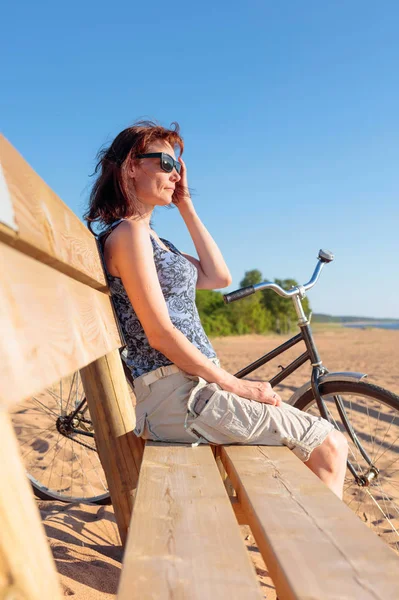 Mulher de meia-idade veio em uma bicicleta para a praia e descansar sentar — Fotografia de Stock