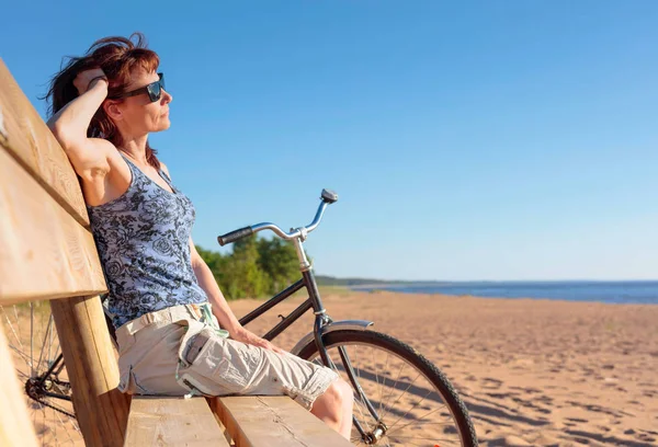 Középkorú nő jött egy bicikli a strandon és a pihenő ülni — Stock Fotó