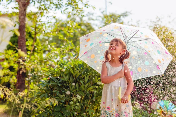 アンブレルと夏の雨の下で庭で幸せな小さな女の子 — ストック写真