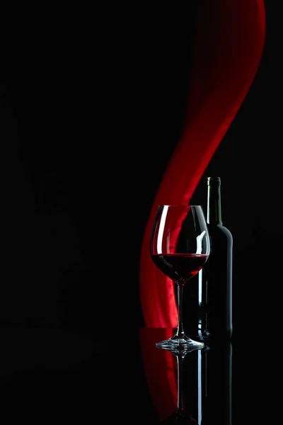 Wineglass i butelka czerwonego wina na czarnym odblaskowym oświetlenie tła — Zdjęcie stockowe