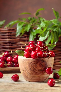 Bahçede ahşap bir masa üzerinde ahşap bir kase kırmızı tatlı kiraz.