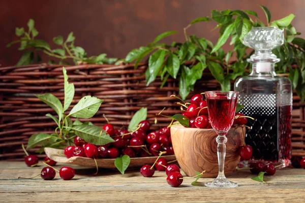 Licor de cereja e cerejas vermelhas em uma tigela de madeira em uma mesa de madeira — Fotografia de Stock