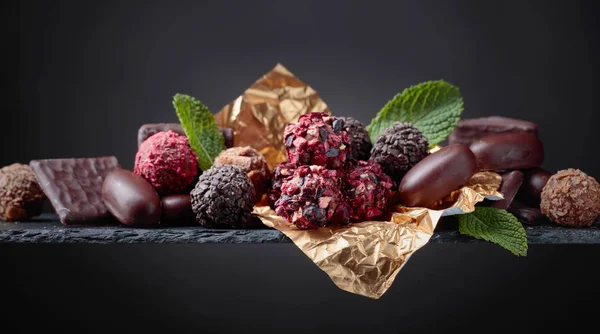 Various chocolates with mint leaves on a black background. — Stock Photo, Image