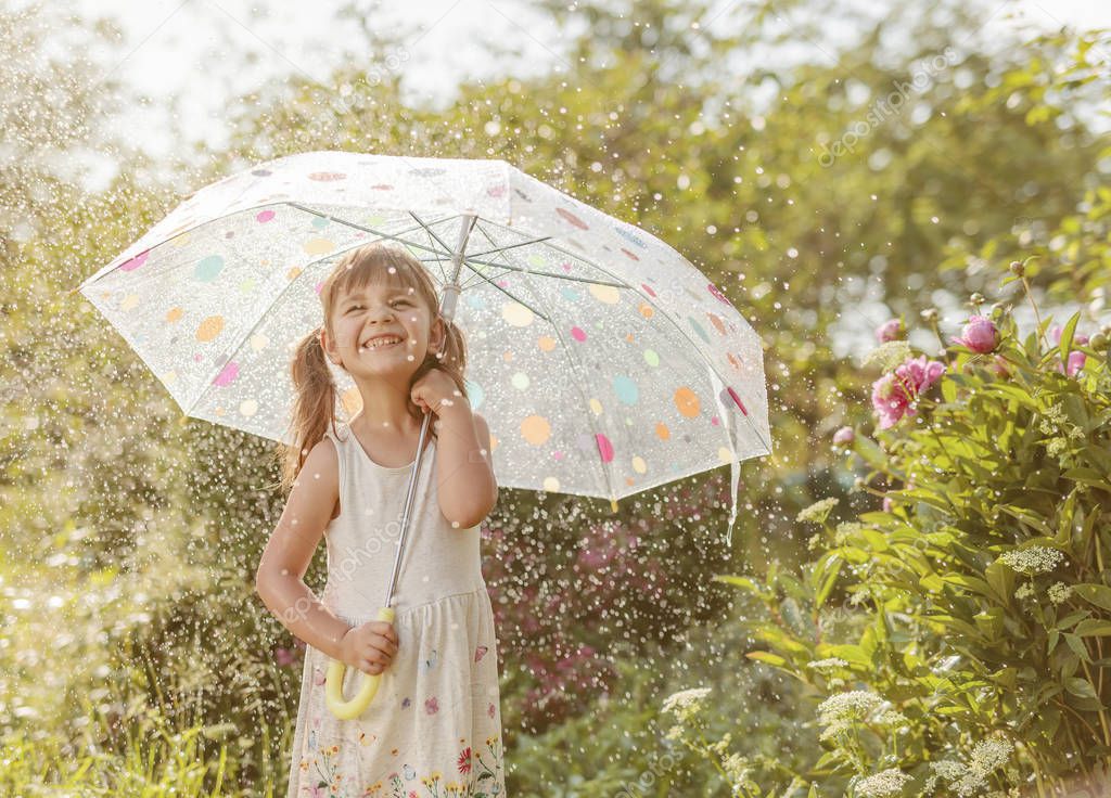 Happy little girl in garden under the summer rain with an umbrel