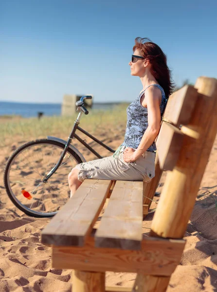 Mujer de mediana edad llegó en una bicicleta a la playa y sentarse a descansar —  Fotos de Stock