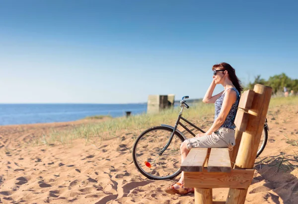 Mujer de mediana edad llegó en una bicicleta a la playa y sentarse a descansar —  Fotos de Stock