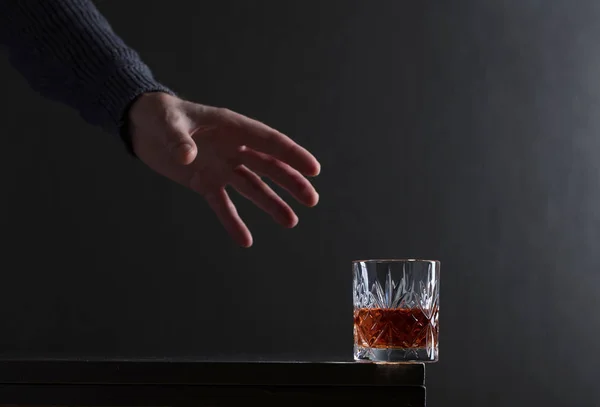 Iemands hand bereikt voor een glas alcohol. — Stockfoto