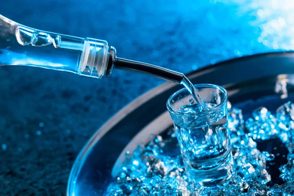 Wodka in ein Glas mit blauer Hintergrundbeleuchtung gegossen. — Stockfoto