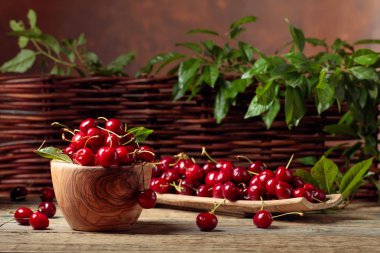 Bahçede ahşap bir masa üzerinde ahşap bir kase kırmızı tatlı kiraz.