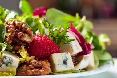 Mavi peynir dilimleri ile yeşil salata, ahududu ve fındık.