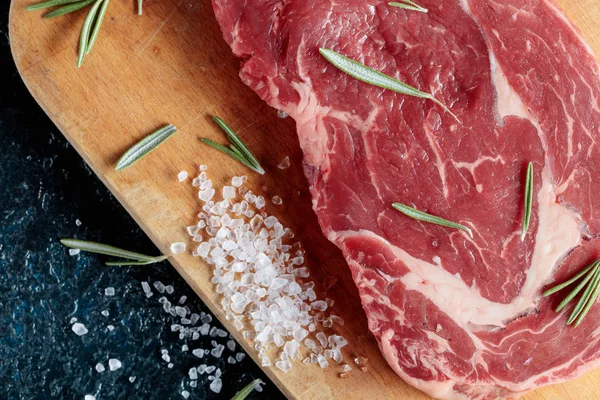 Verse rauwe biefstuk op een houten bord met rozemarijn en zee zout. — Stockfoto