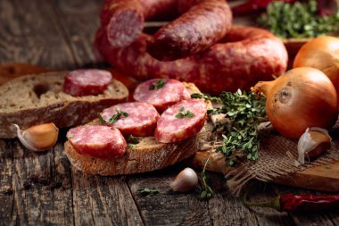 Dry-cured sausage with bread and spices on a old wooden table. clipart