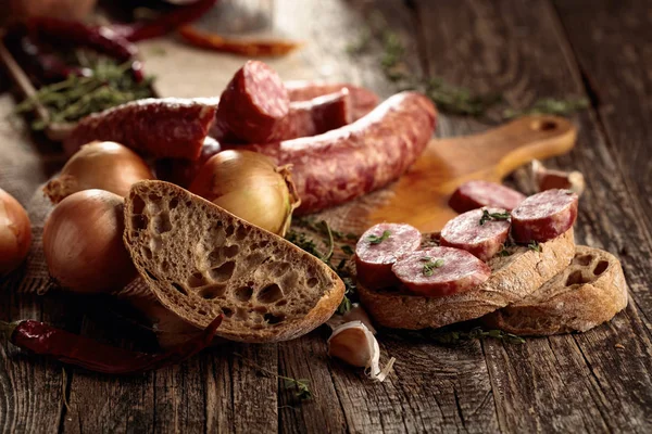 Dry-cured sausage with bread and spices on a old wooden table. — Stock Photo, Image