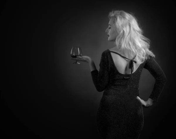 Piękna Blondynka w czarnej sukni wieczorowej z snifter brandy. — Zdjęcie stockowe