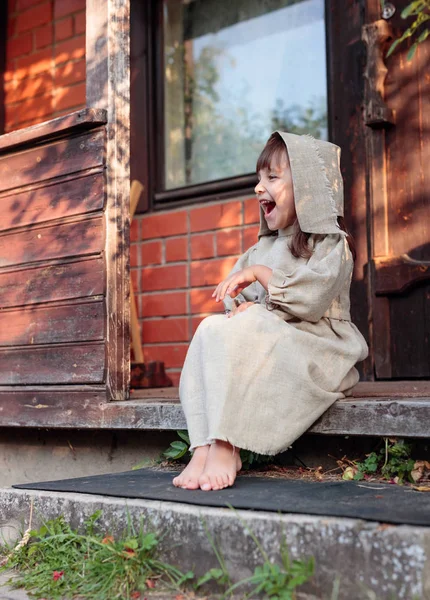 Little  barefoot girl in a old canvas dress on the threshold of — Stock Photo, Image