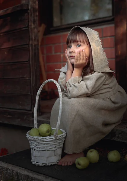 Мечтающая девушка с яблоками летним вечером возле старого дома — стоковое фото