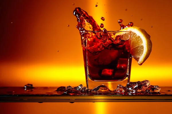 Stukje citroen dat in een glaasje Cola valt. — Stockfoto
