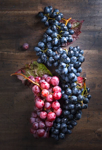 Rote und blaue Trauben mit Blättern auf einem alten Holztisch. — Stockfoto