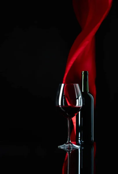 Verre à vin et bouteille de vin rouge sur un fond réfléchissant noir — Photo