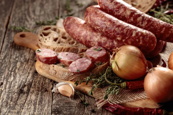 Dry-cured sausage with bread and spices on a old wooden table.