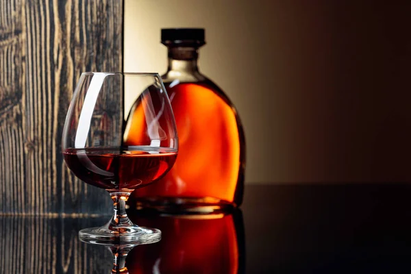 Vidrio y botella de brandy sobre fondo negro reflectante . —  Fotos de Stock