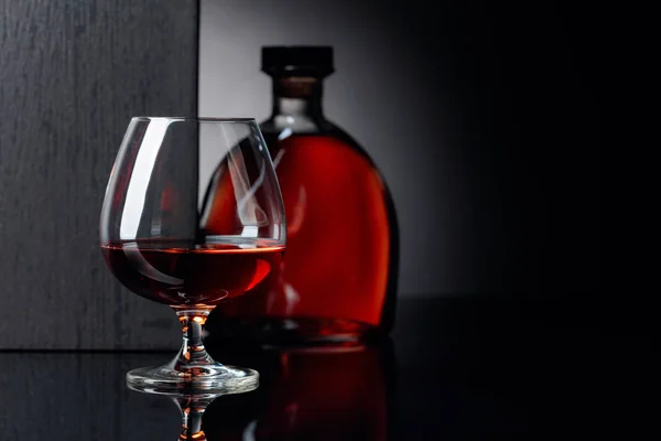 Vidrio y botella de brandy sobre fondo negro reflectante . — Foto de Stock