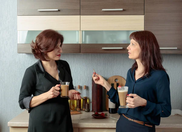 Twee vriendinnen praten en drinken koffie in de keuken. — Stockfoto