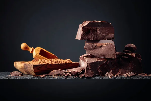 Zwarte chocolade en houten schaaltje met cacaopoeder op een donkere rug — Stockfoto