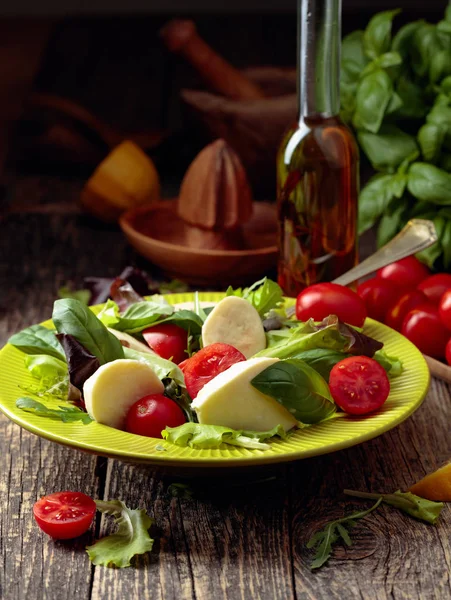 Ensalada verde con mozzarella, tomate y albahaca en plato verde sobre —  Fotos de Stock