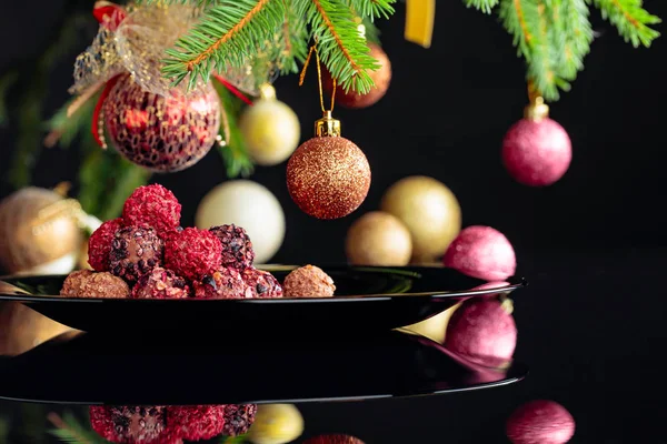 Chocolate truffles on a black plate and Christmas tree. — Stock Photo, Image