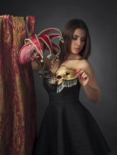 Mujer atractiva joven en un vestido negro con máscaras de carnaval . —  Fotos de Stock