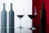 Láhve a sklenice červeného vína na černém odrazném pozadí