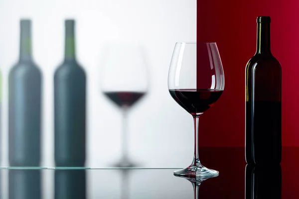 Бутылки и бокалы красного вина на черном отражающем фоне — стоковое фото