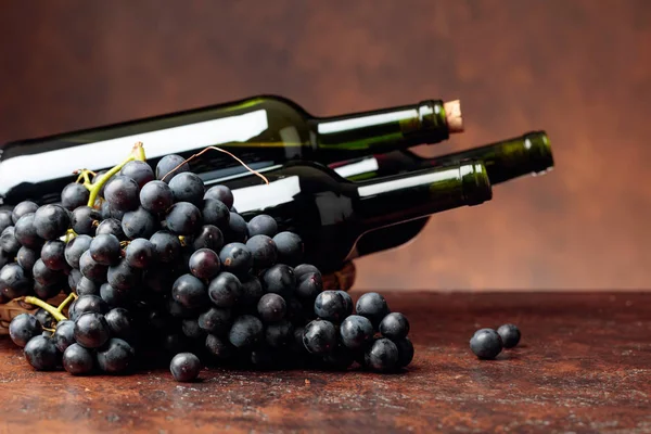 Sappige blauwe druiven en flessen rode wijn op een bruine achtergrond. — Stockfoto