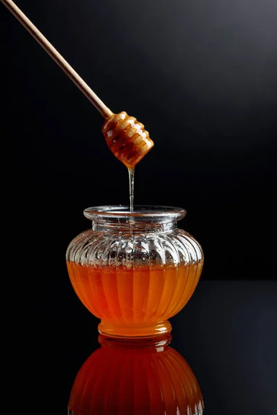 黒い反射の背景に瓶の蜂蜜. — ストック写真