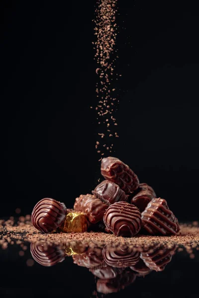 Doces de chocolate em um fundo preto polvilhado com chocolate — Fotografia de Stock