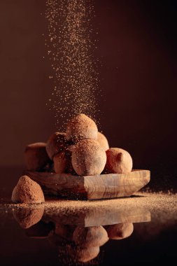 Çikolatalı trüf mantarı kakao tozu serpiştirilmiş küçük ahşap tabakta.
