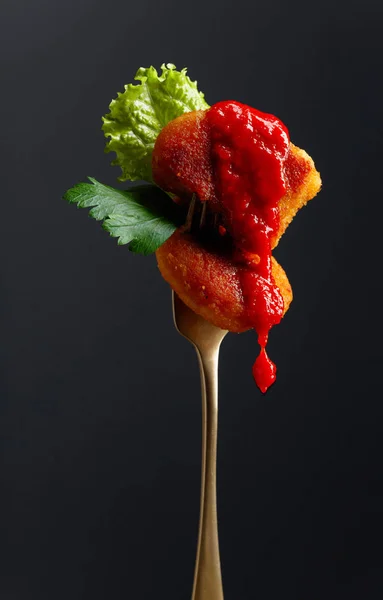 Fried chicken nuggets with ketchup, parsley and salad on a fork.