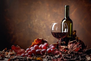 Kurumuş asma yapraklı bir masada bir şişe kırmızı şarap.