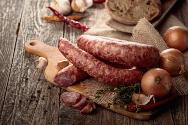Dry-cured sausage with bread and spices on a old wooden table. clipart