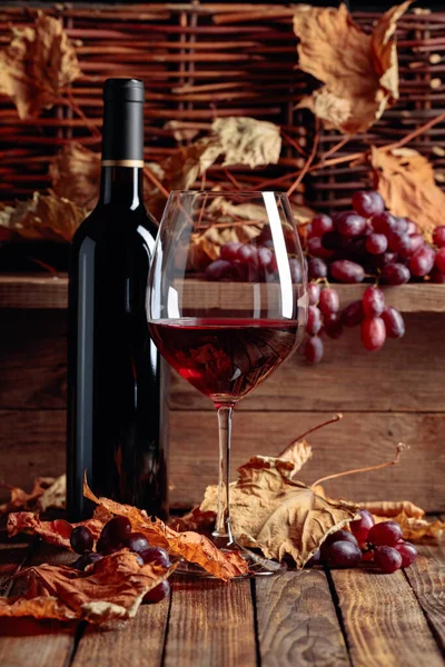 赤ワインとブドウのグラスとボトル 古い木製のテーブルの上にワイン ブドウ 乾燥ブドウの葉 — ストック写真