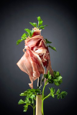 Çatalla maydanozlu ince dilimlenmiş jambon. Geleneksel İtalyan mutfağı. Siyah arkaplan.