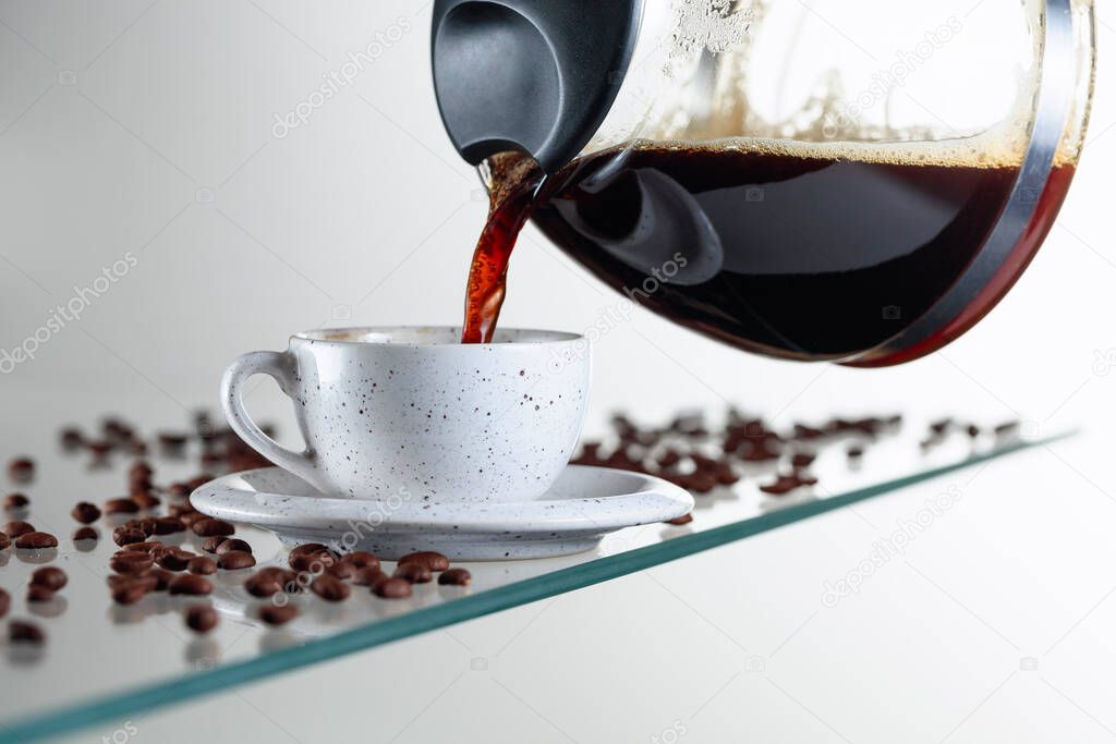 Black coffee in a ceramic cup on a glass table. Coffee is poured from the coffee maker into a cup. Copy space.