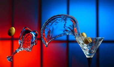Bardakta martini ve yeşil zeytin. Renkli bir arkaplanda sıçramalar. Boşluğu kopyala.