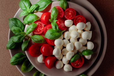Domatesli Caprese salatası, kahverengi arka planda mini mozzarella ve fesleğen. İtalyan yemeği ve sağlıklı vejetaryen diyeti. Boşluğu kopyala, üst görünüm.