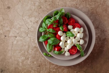 Domatesli Caprese salatası, kahverengi arka planda mini mozzarella ve fesleğen. İtalyan yemeği ve sağlıklı vejetaryen diyeti. Boşluğu kopyala, üst görünüm.