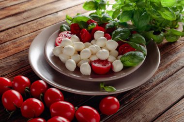 Domatesli Caprese salatası, eski ahşap bir masada mini mozzarella ve fesleğen. İtalyan yemeği ve sağlıklı vejetaryen diyeti.