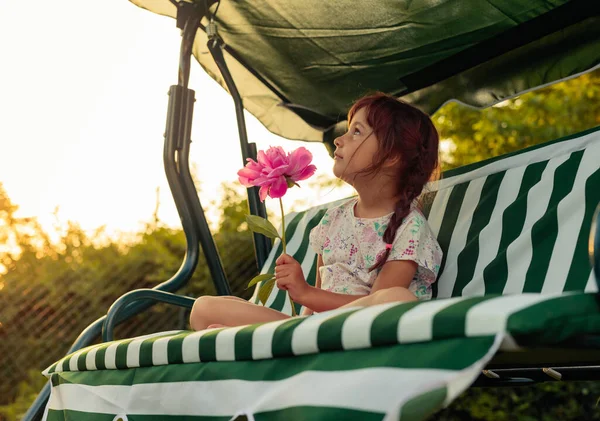 ピンクの牡丹の小さな女の子が庭のベンチに座っています 庭の夏の夜 — ストック写真