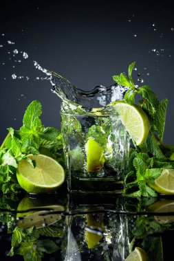 Limonlu kokteyl ve siyah yansıtıcı arka planda nane. Limon dilimi bardağa dökülür..